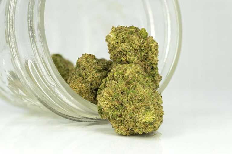 Cannabis buds spilling from glass jar on white background.