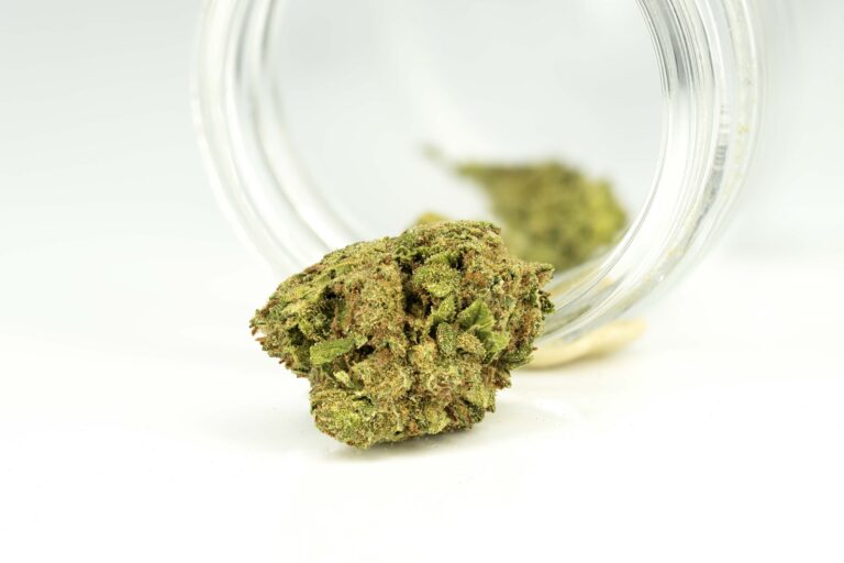 Cannabis bud spilling from jar on white background.