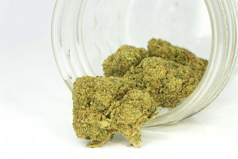 Cannabis buds spilling from jar on white background.