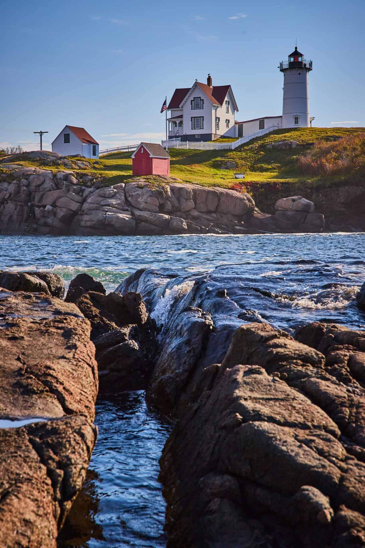 Lab-tested THCa flower shipped to Maine. rocky-coast-with-waves-filling-cracks-lighthouse-background-maine